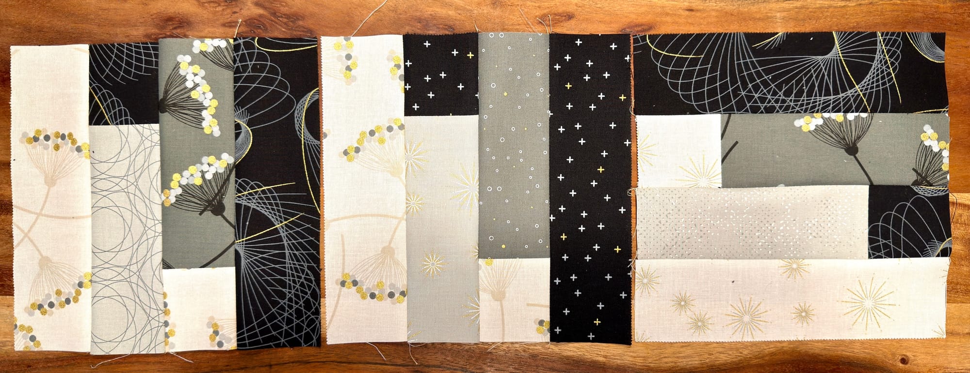 Three jellyroll blocks with fabric that has a mix of flowers, stars, plus signs, and mathematical curves. Two blocks are the same, the other is reflected.