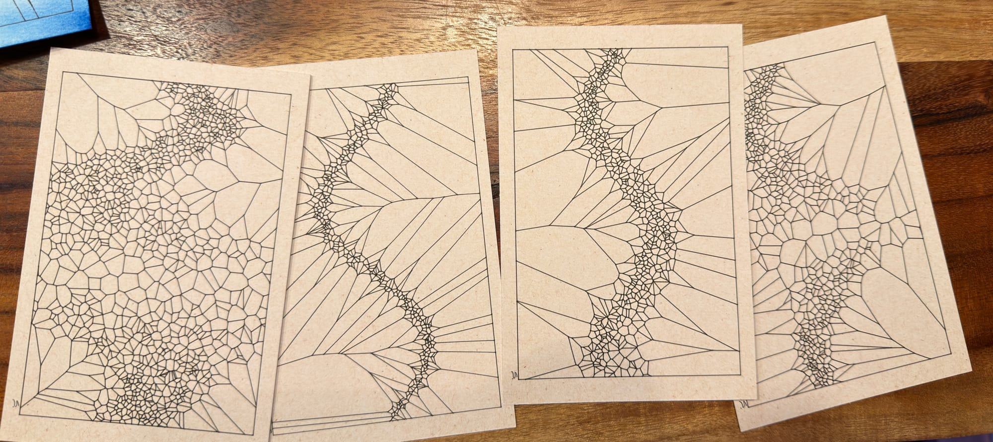 four postcards with black pen curves made of voironoi areas in sinusoidal patterns with some ruptures of larger areas on some of them . the paper is off white and the table they are on is wood. 
